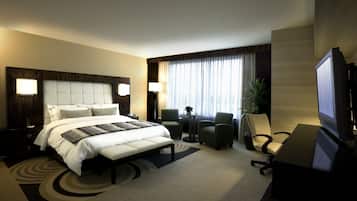 Ein Hotelzimmer mit einem großen Bett, zwei Sesseln, einem Schreibtisch mit Computer und einem Fernseher.