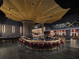 A bar area with a curved counter, bar stools, and a ceiling with a unique design.