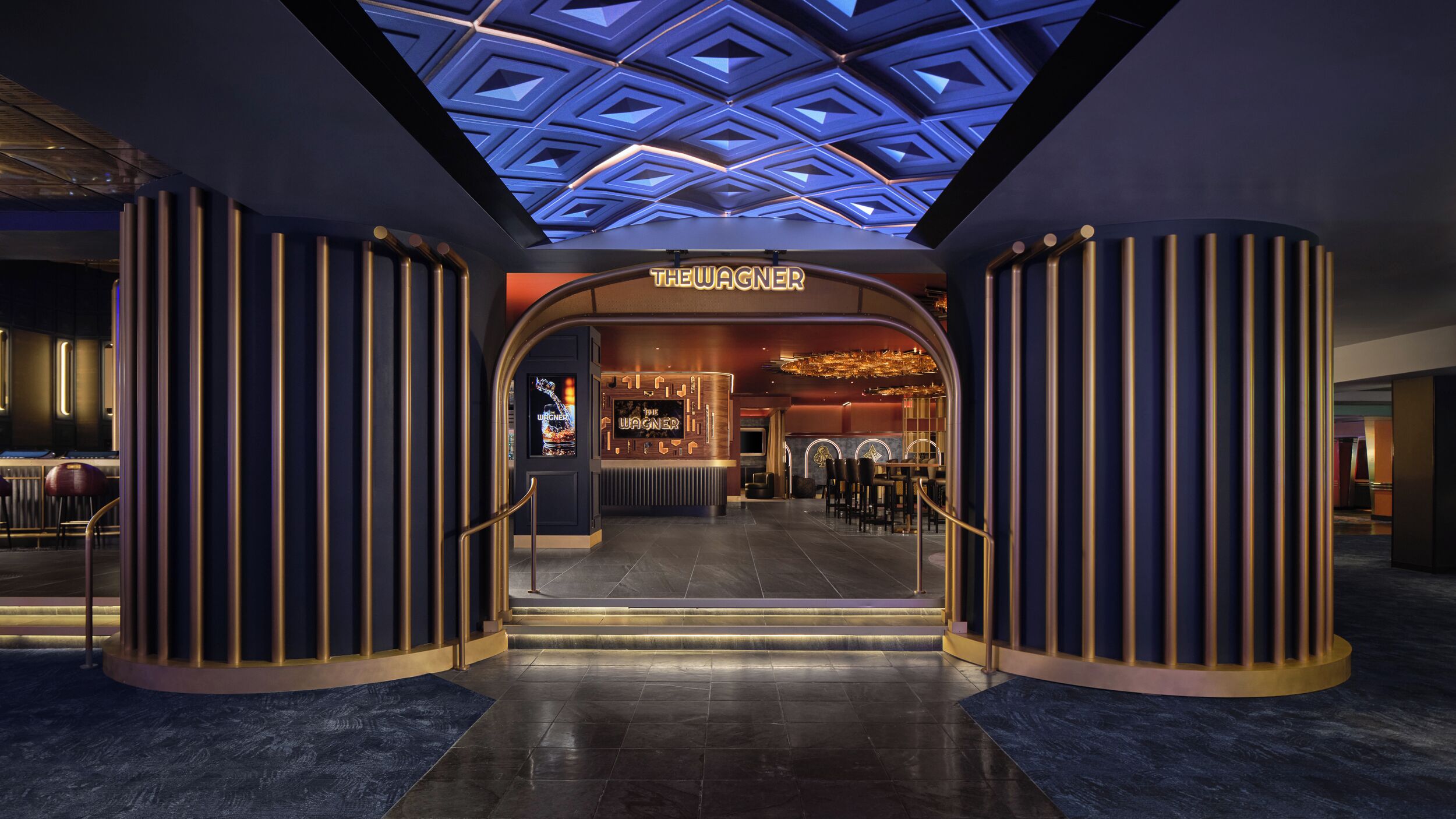 Un hall d’hôtel doté d’un plafond au design géométrique, d’une entrée principale avec une enseigne et d’un espace bar.