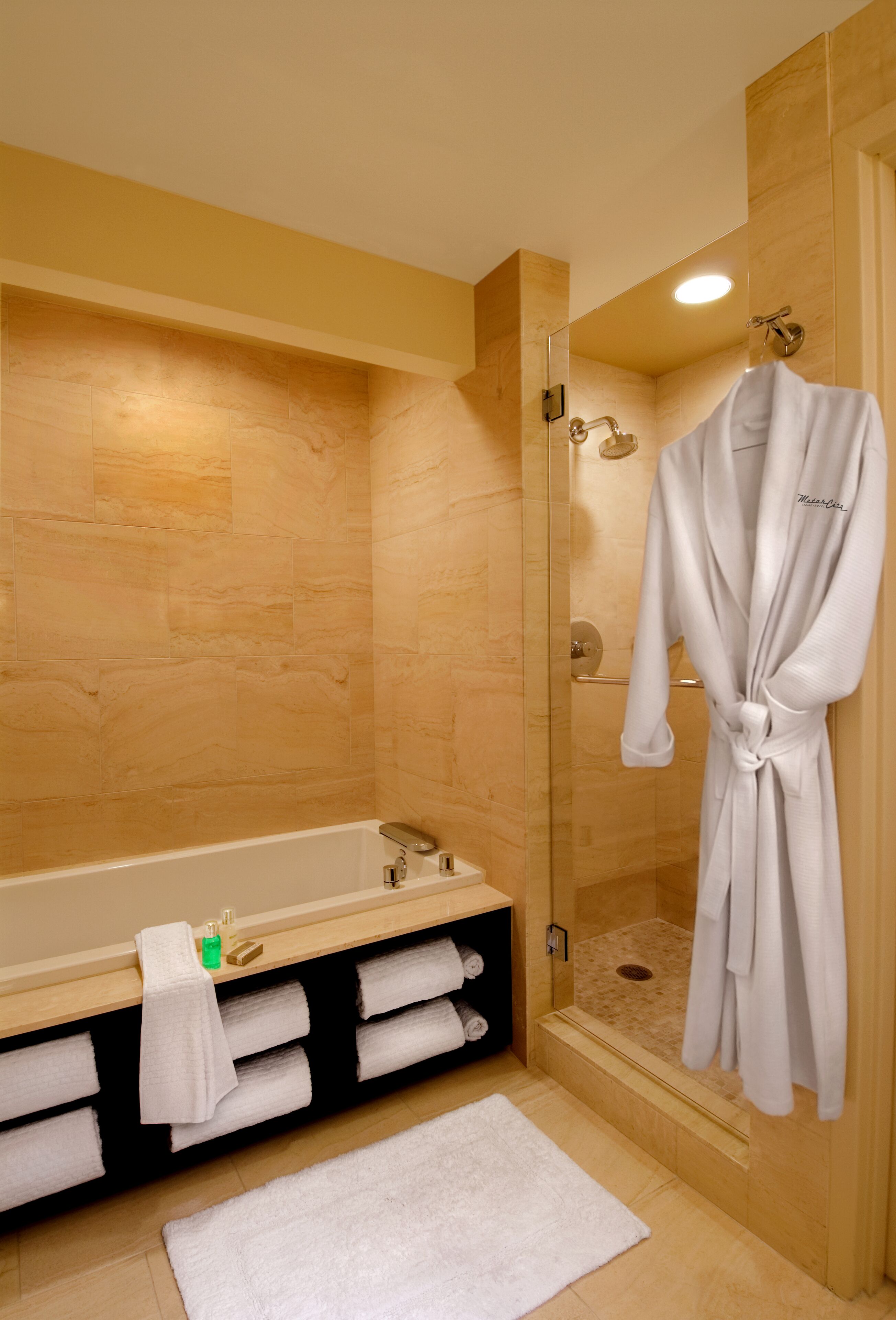A modern bathroom with a glass-enclosed shower, a bathtub, and a robe hanging on the wall.
