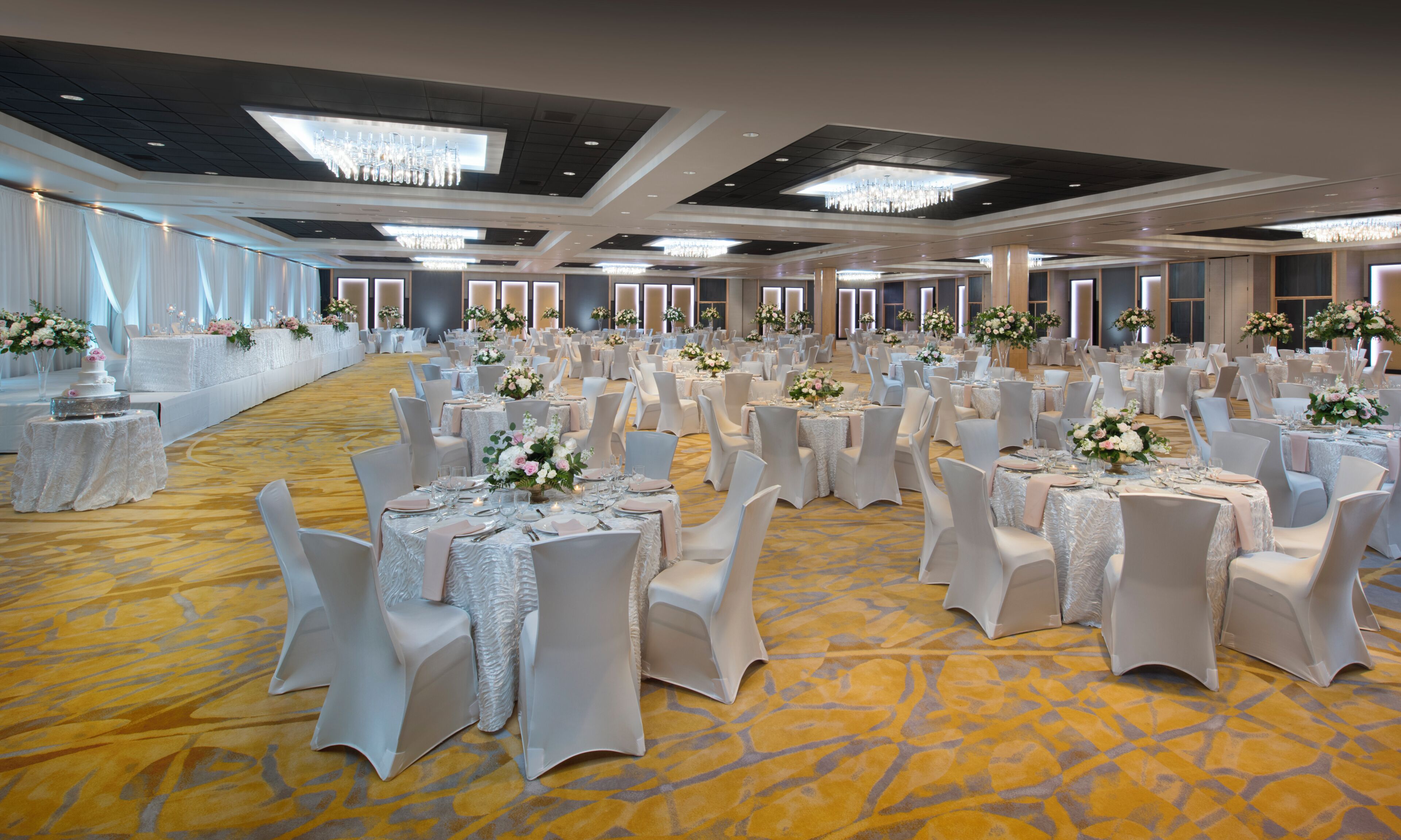 A banquet hall with round tables, white chairs, and floral centerpieces.
