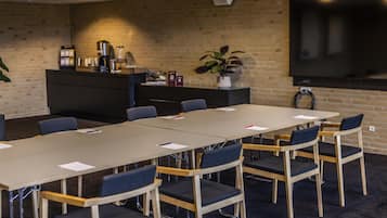 A conference room with a long table, chairs, a coffee machine, a plant, and a TV on the wall.