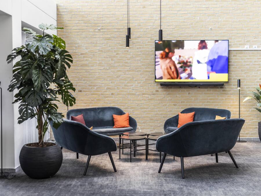 A modern lounge area with a brick wall, a flat-screen TV mounted above a seating area, and a large potted plant.