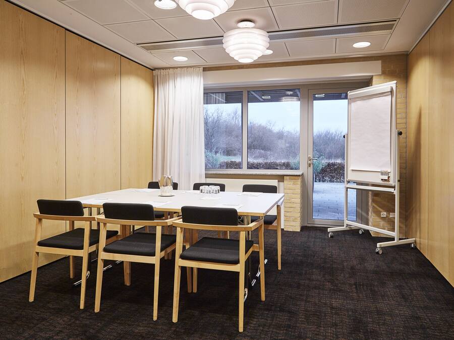 A conference room with a large table, six chairs, a whiteboard, and a view through the windows.