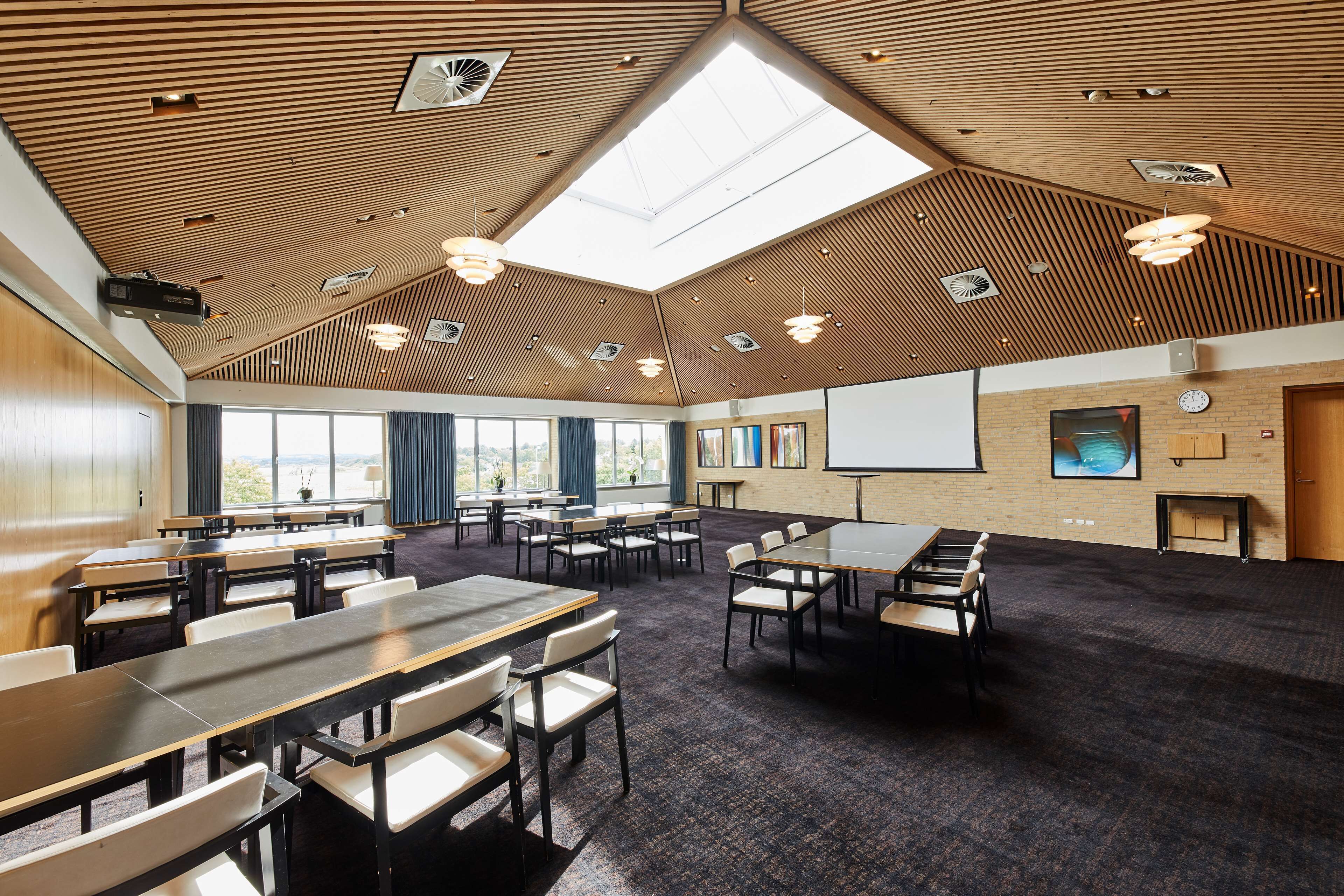 A conference room with a high ceiling, wooden paneling, and a skylight. Tables and chairs are arranged for meetings.