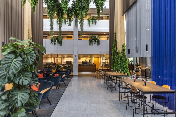 A spacious indoor area with multiple seating arrangements, including tables and chairs, and hanging plants. - Scandic Opus Horsens (Horsens)