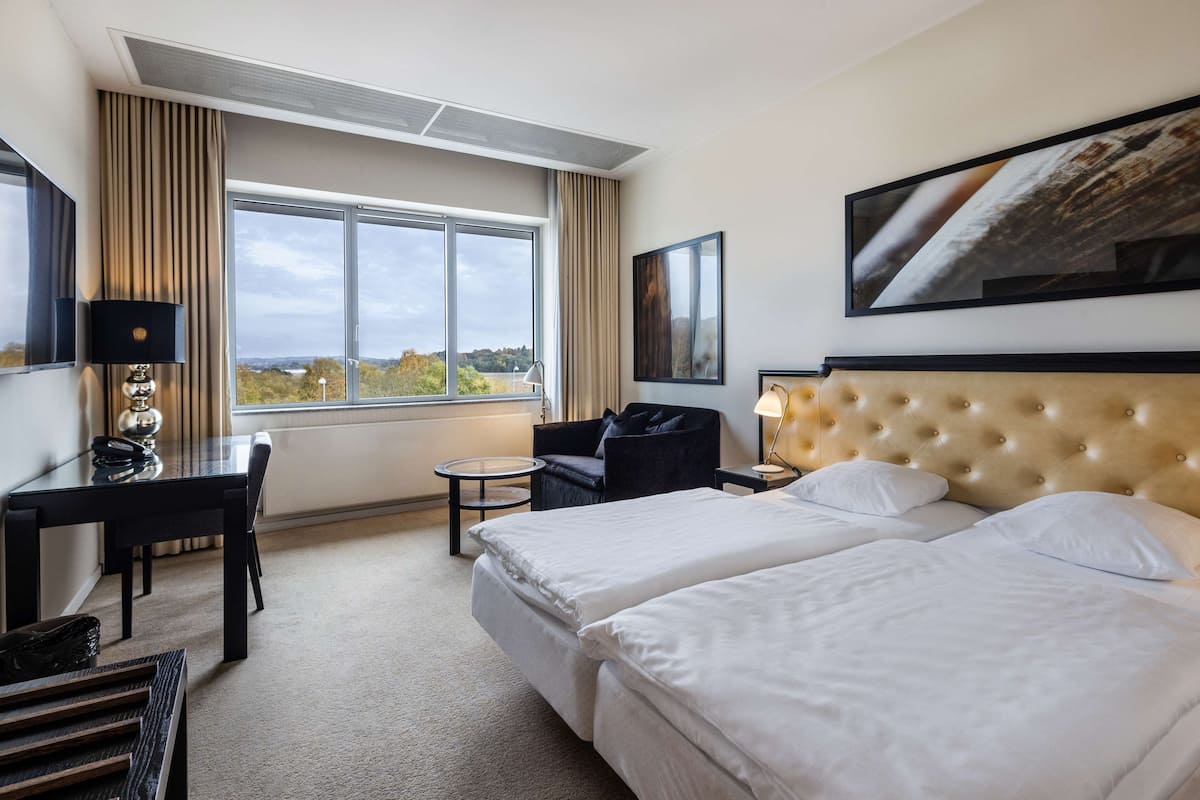 Une chambre d’hôtel avec une grande fenêtre, un lit, un bureau, une chaise et une petite table.