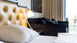 Una habitación de hotel con cabecera acolchada, una lámpara de noche, un almohadón blanco y ropa de cama blanca.