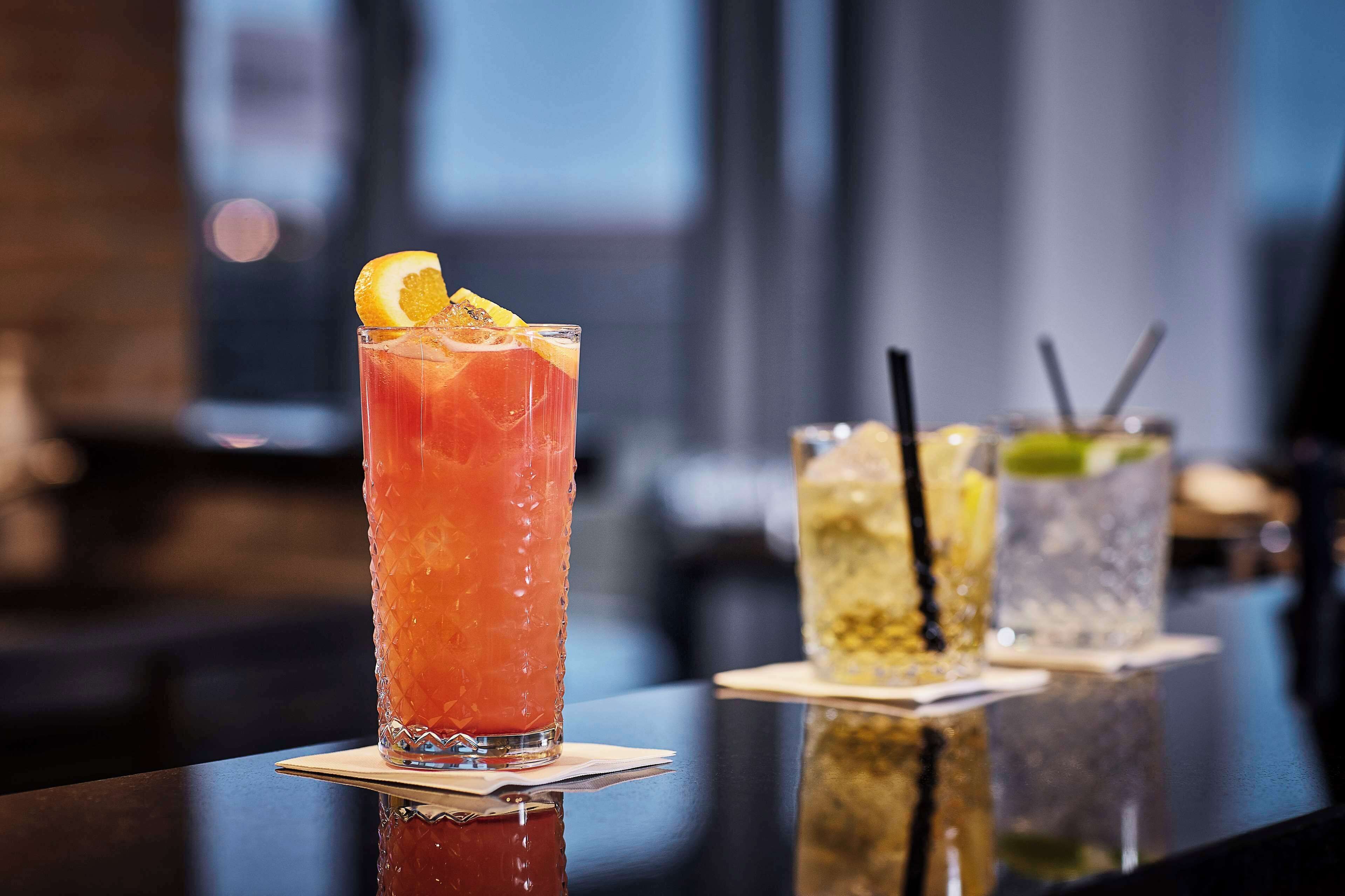 Un bar con una variedad de bebidas, incluyendo un vaso alto con una bebida roja adornada con una rodaja de naranja.