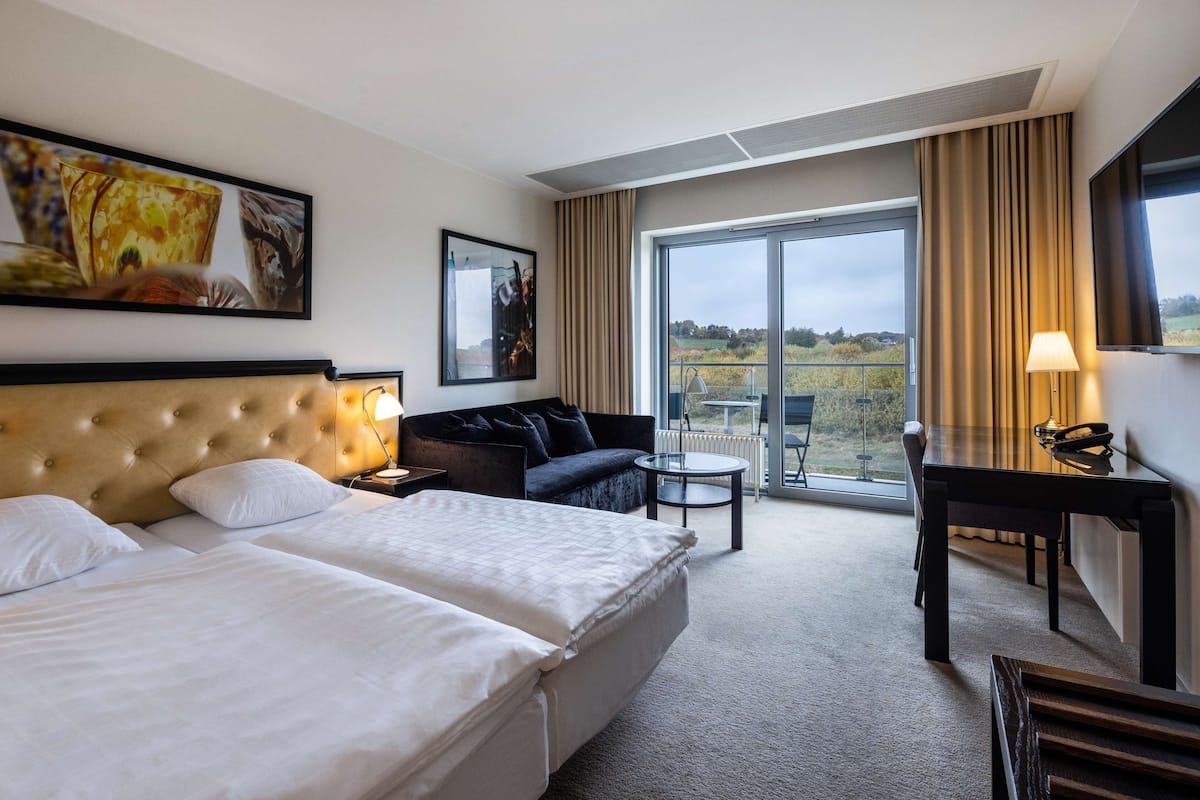 Une chambre d’hôtel avec deux lits, un canapé, un bureau et un balcon avec vue.