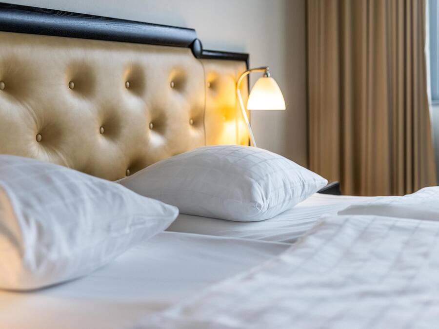 A bed with a tufted headboard, white pillows, and a bedside lamp.