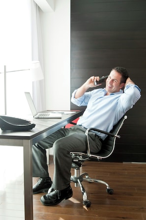 A man sitting in a modern office chair with a laptop, a telephone, and a black briefcase on a desk. - Fiesta Inn Express Ciudad Obregón (Cajeme)