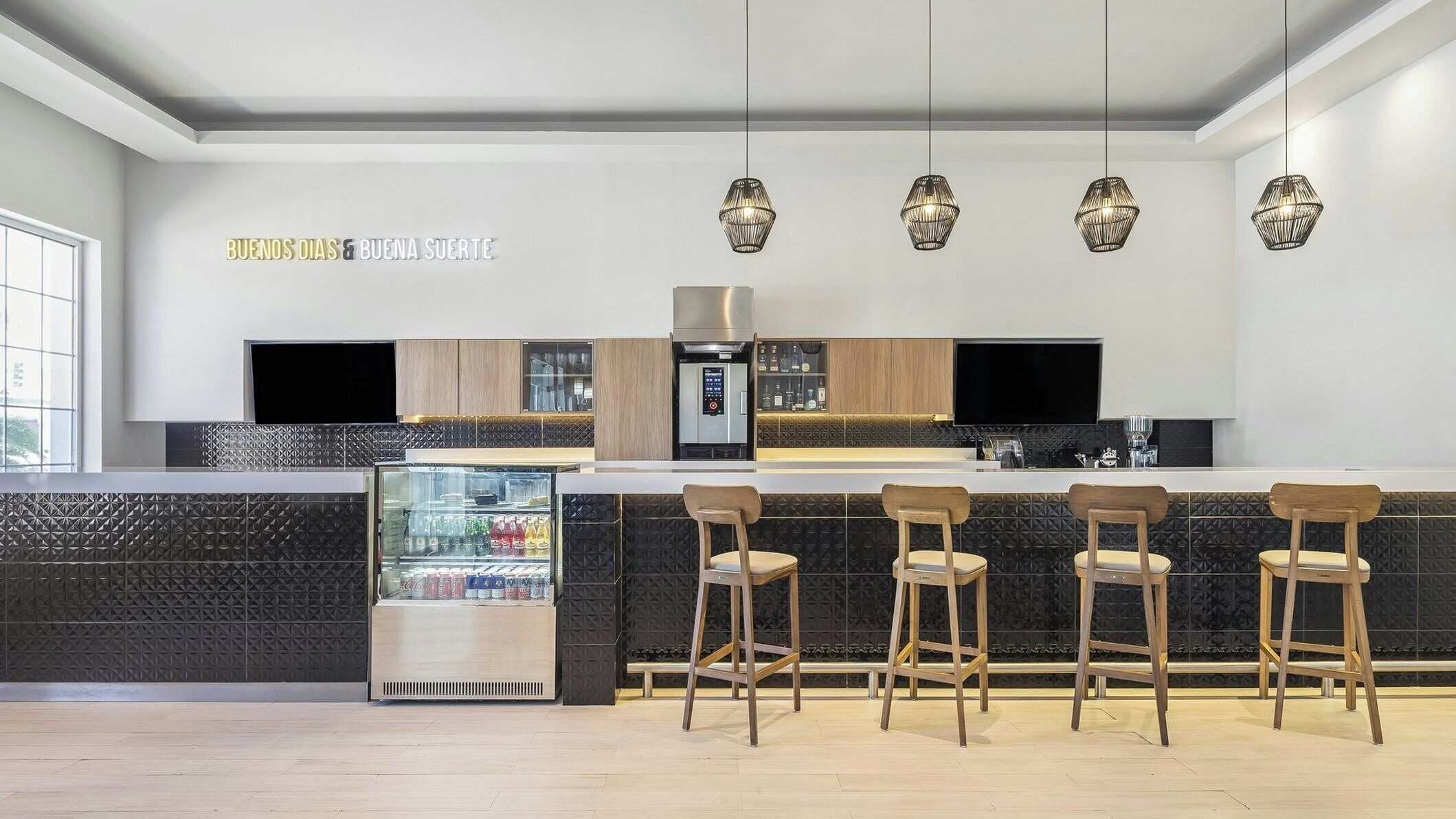 A modern kitchen with a built-in refrigerator, a microwave, and a coffee machine. There are four wooden bar stools and a large window providing natural light.