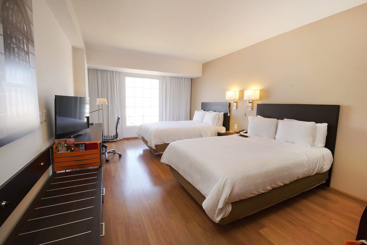 Hotellihuone, jossa on kaksi sänkyä, televisio, työpöytä ja ikkuna, jossa on verhot.