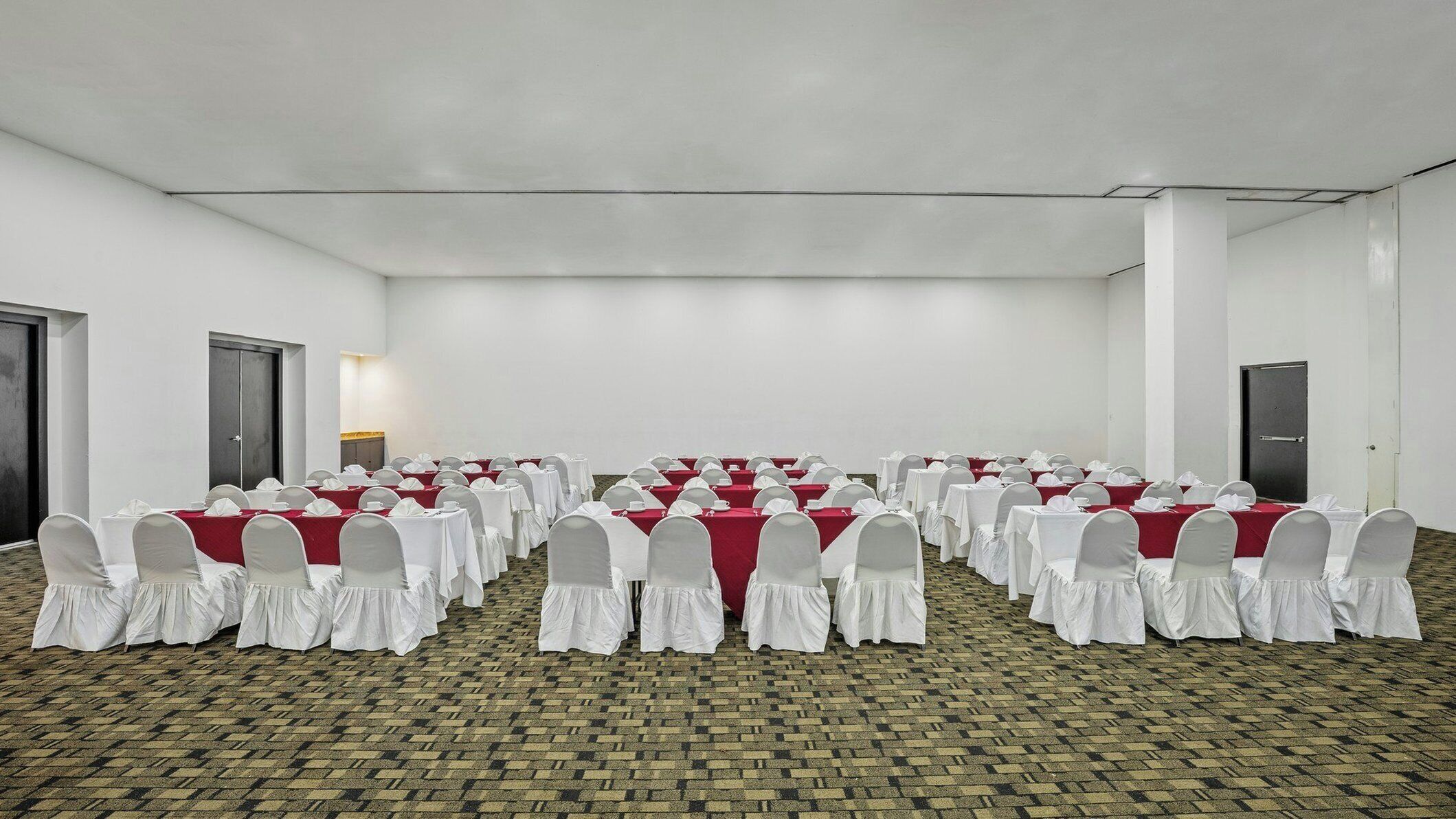 A conference room with rows of tables and chairs, carpeted floor, and white walls.
