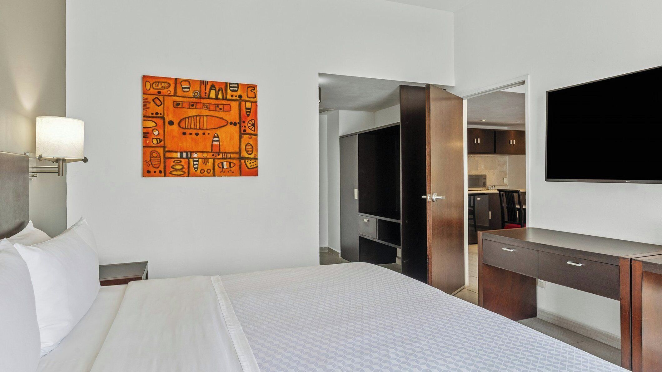 A hotel room with a bed, a TV, a wardrobe, and a painting on the wall.