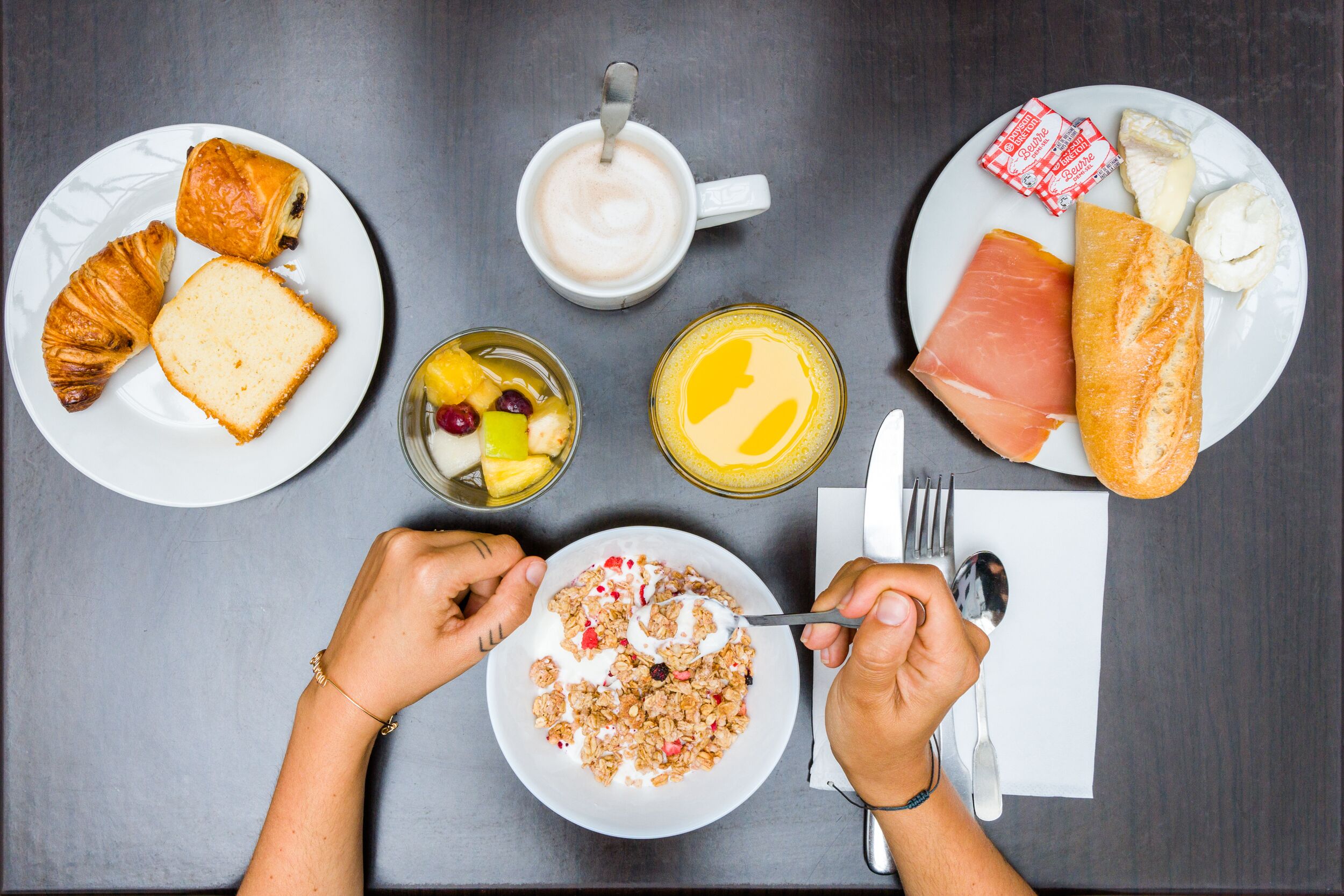 Un desayuno con cruasanes, una taza de café, una fuente de salmón ahumado, queso y un bol de cereal.