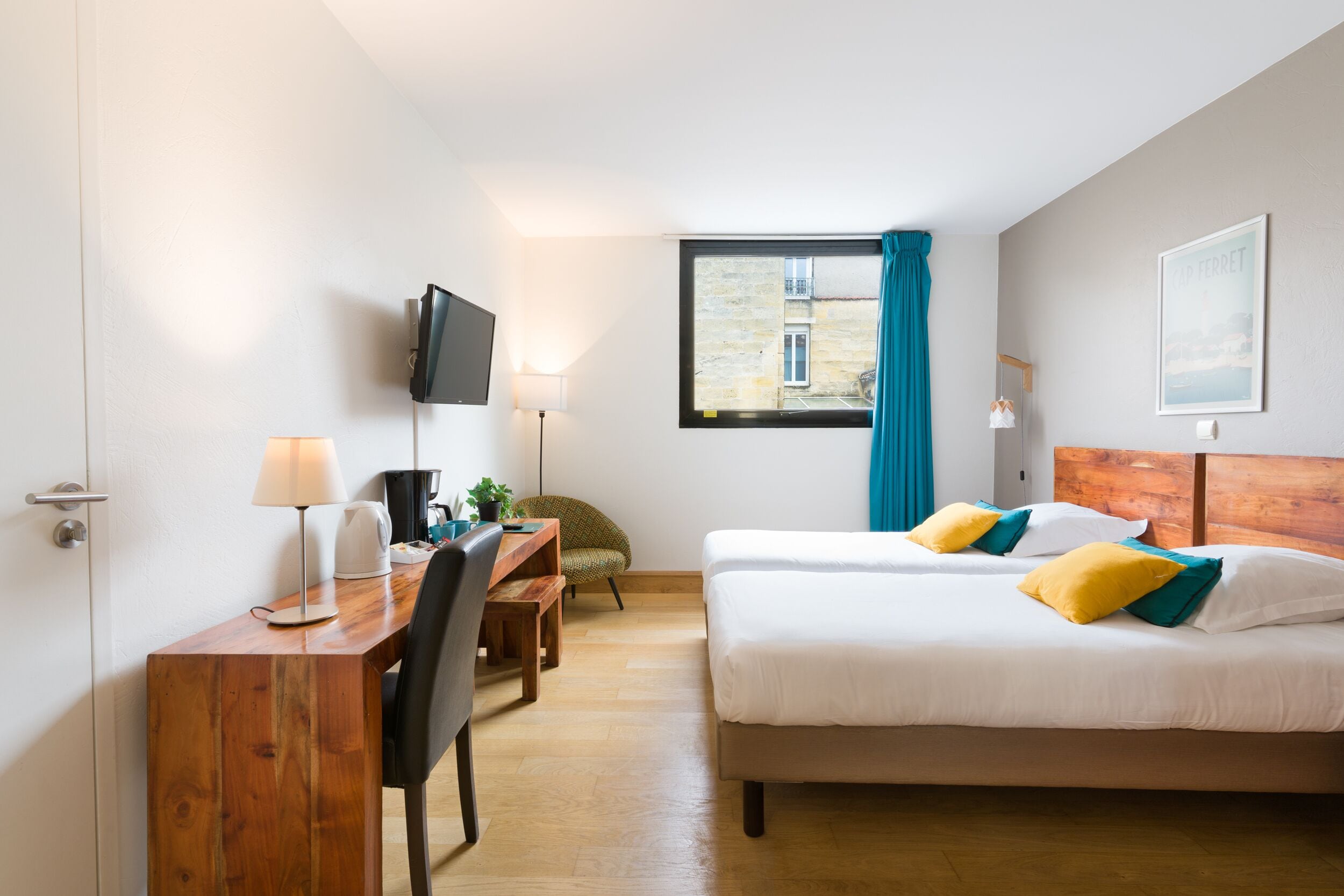 A hotel room with two beds, a desk with a chair, a TV, and a window with curtains.