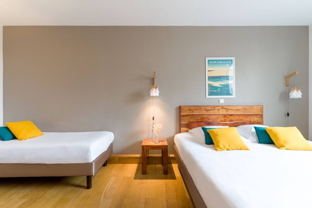 Een hotelkamer met twee bedden, een houten hoofdbord, een klein tafeltje met een lamp en een poster aan de muur.