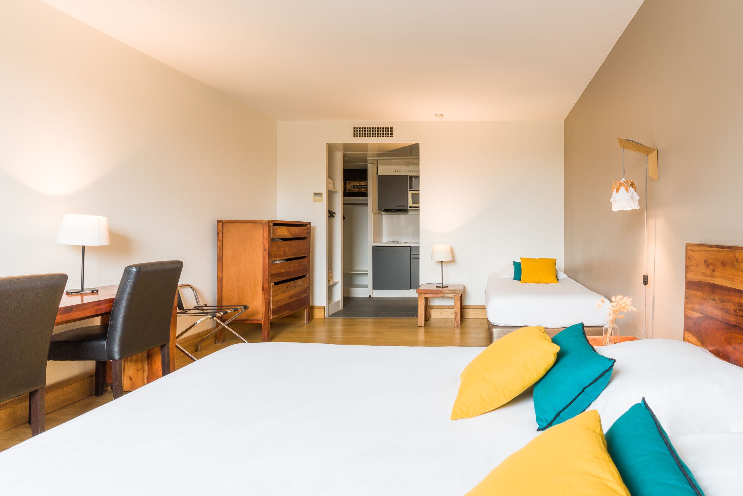 Ein Hotelzimmer mit einem Bett, einem Schreibtisch, einem Stuhl, einem Kleiderschrank und einem kleinen Tisch mit einer Lampe.