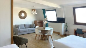 Una habitación de hotel moderna con sofá, mesa de comedor, sillas, televisor y cama.
