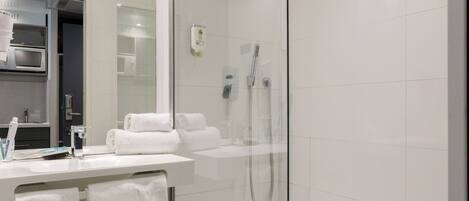 Un baño moderno con ducha envuelta en vidrio, azulejos blancos, un lavamanos con espejo y un inodoro.