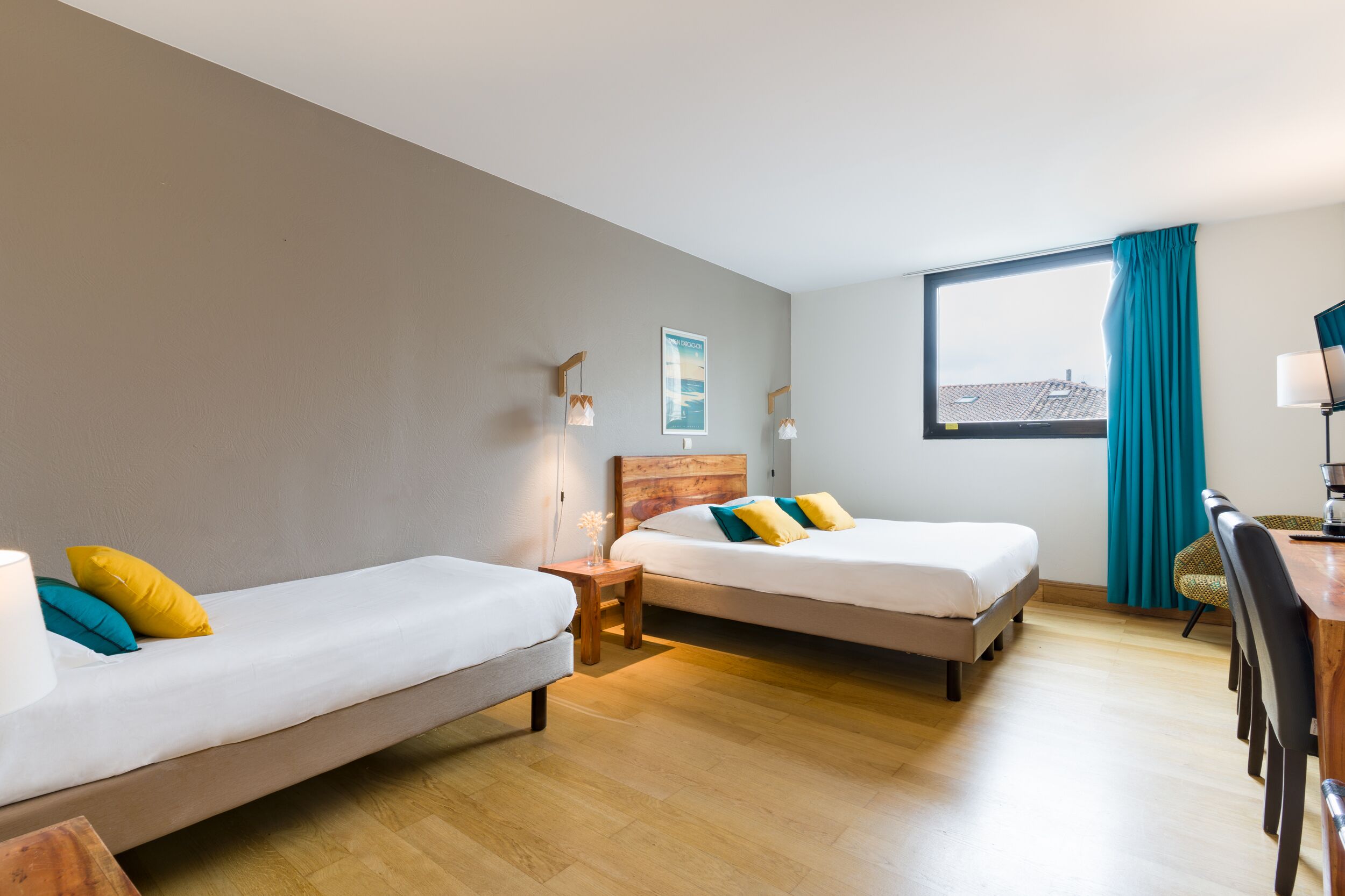 Una habitación de hotel con dos camas individuales, un escritorio de madera, una silla y una ventana con cortinas.