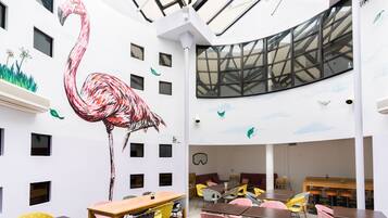 A modern interior with a large wall mural of a flamingo, multiple tables and chairs, and a skylight.