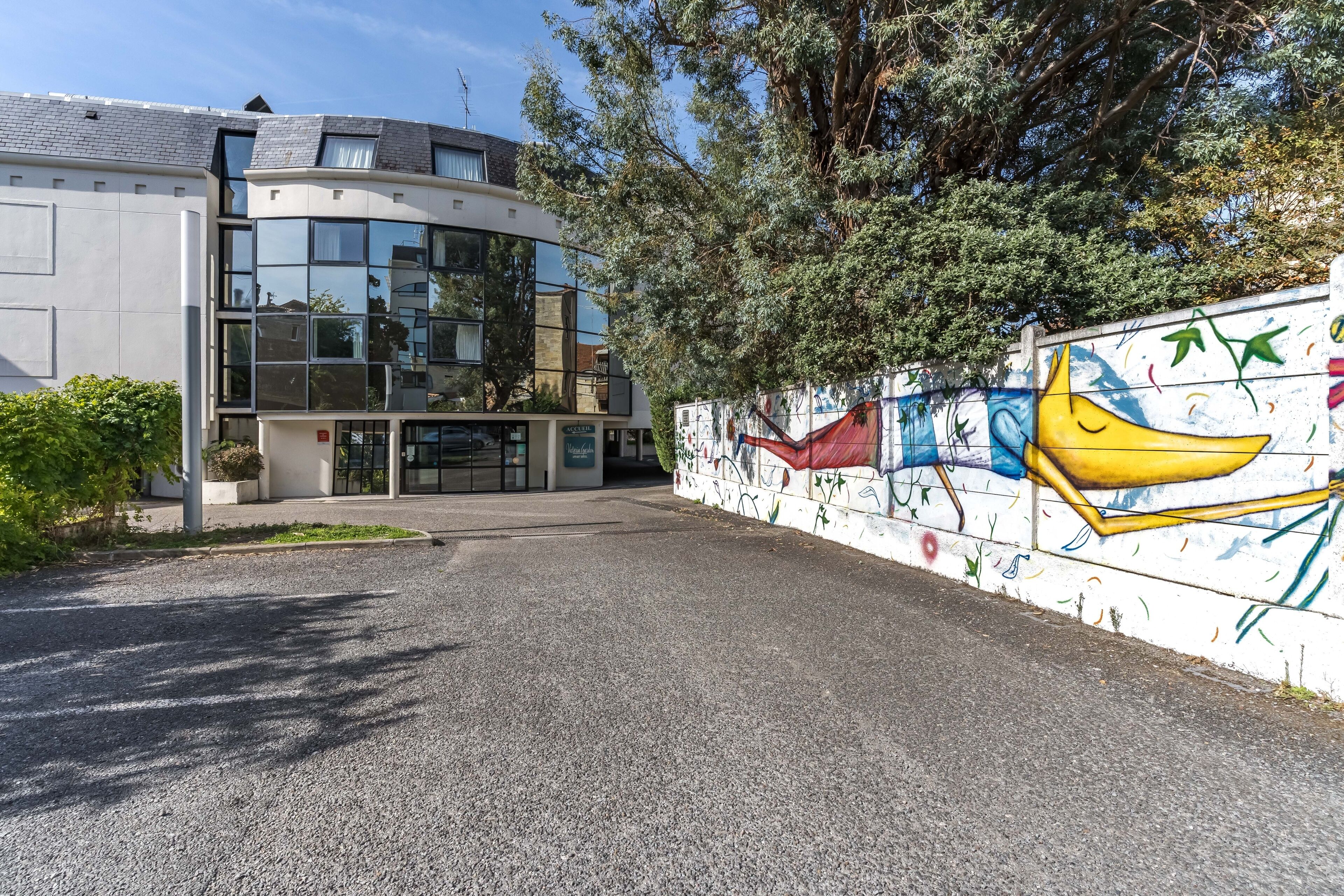 A modern building with a curved facade, large windows, and a mural on the side wall.