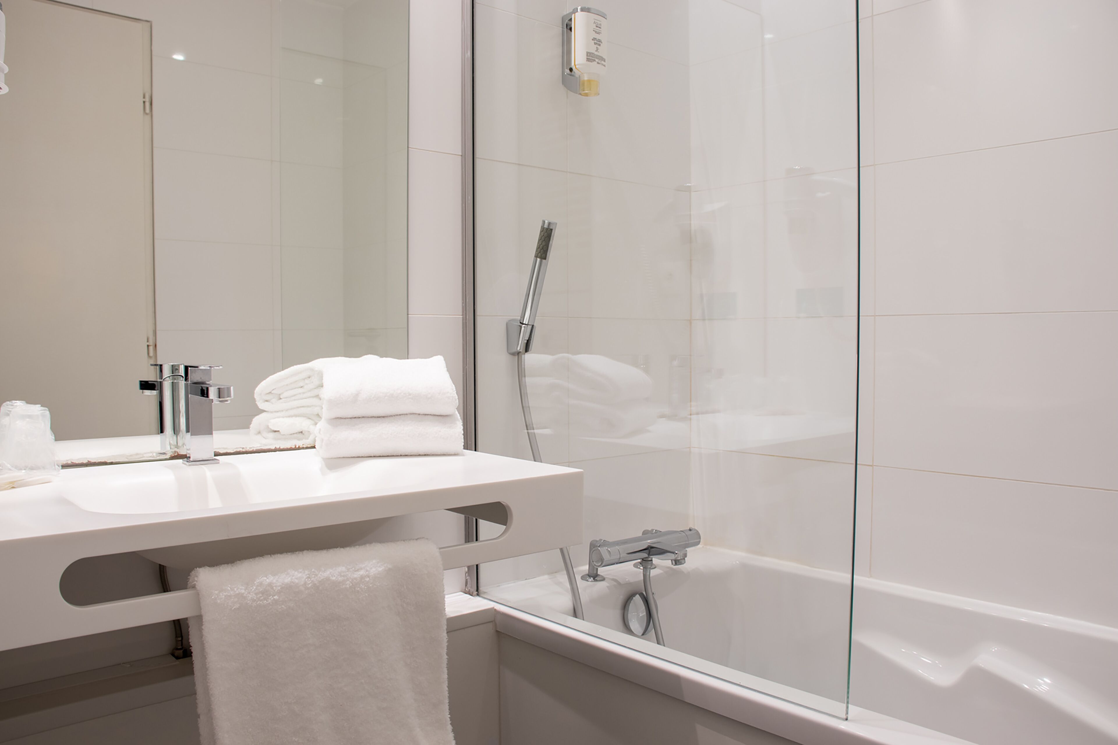A modern bathroom with a glass shower enclosure, a white sink with a mirror, and neatly folded towels.