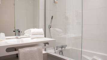 A modern bathroom with a glass shower enclosure, a white sink with a mirror, and neatly folded towels.