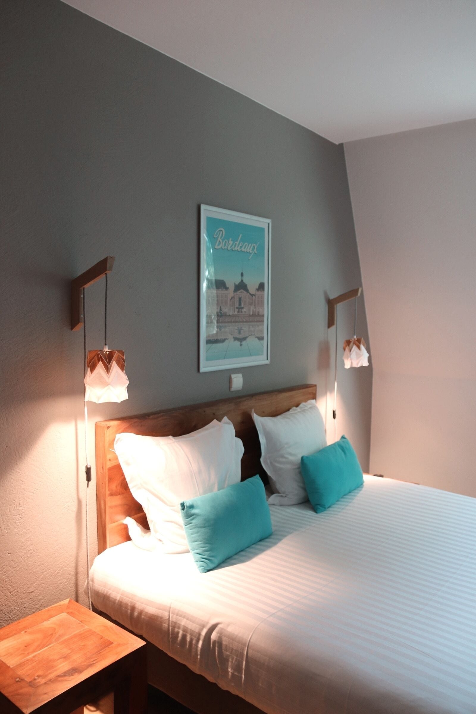 A neatly made bed with white and teal pillows, a wooden headboard, and a framed picture on the wall.