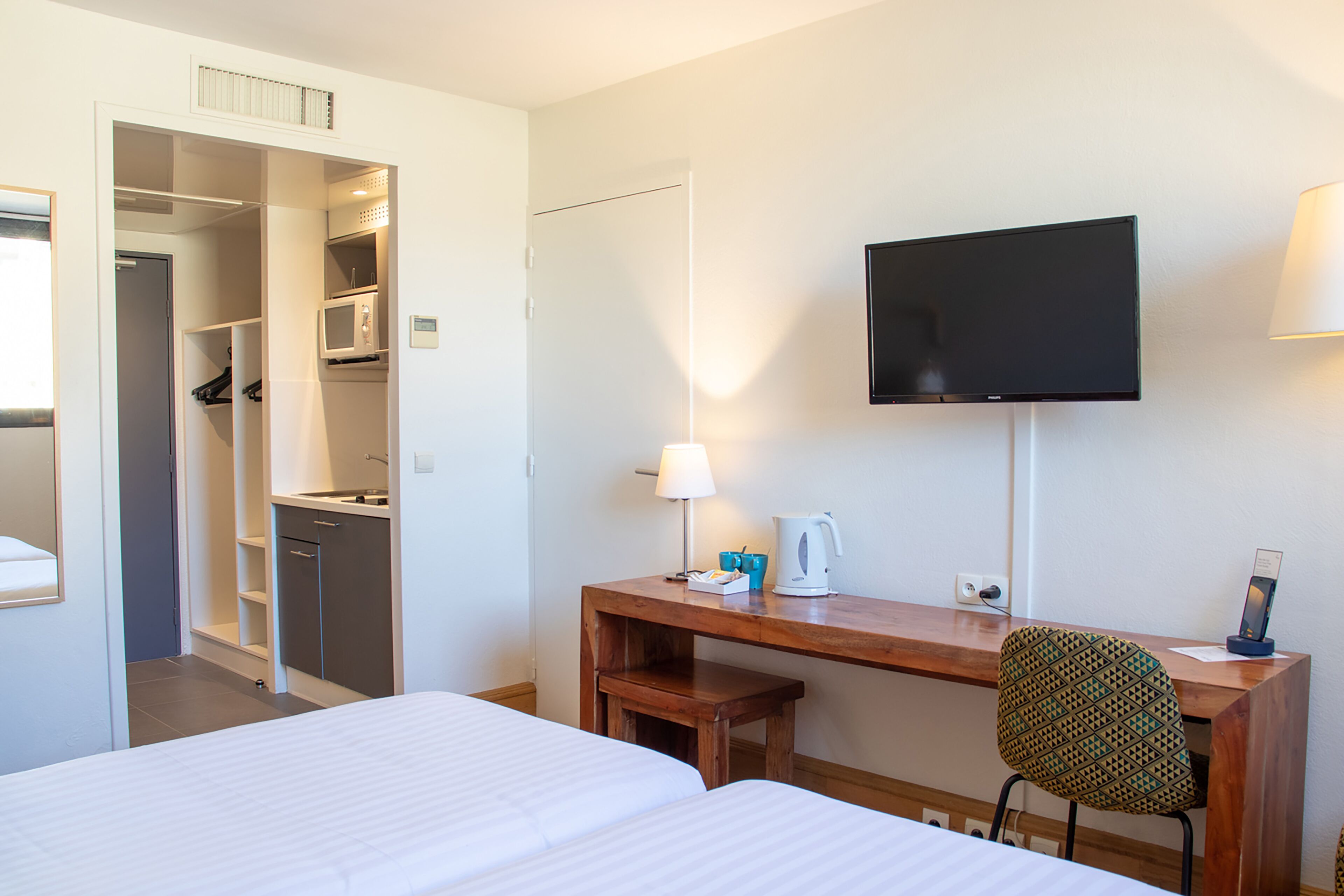 A hotel room with a bed, a desk with a chair, a television, a lamp, and a microwave.