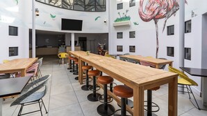 Un interior moderno con una larga barra de madera, varias zonas de estar y un gran mural de un flamenco.