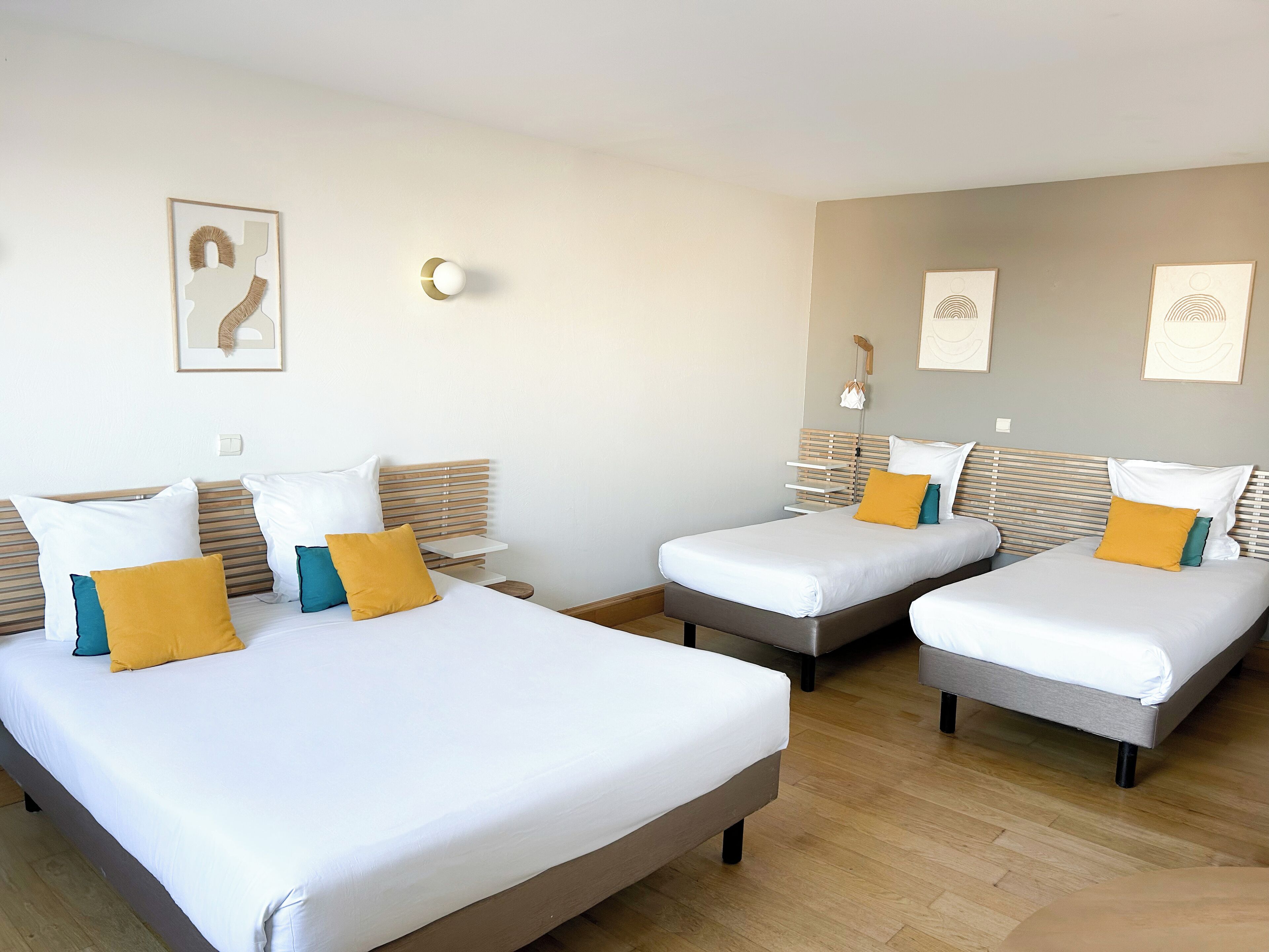 A hotel room with two single beds, a wooden floor, and a neutral color scheme.