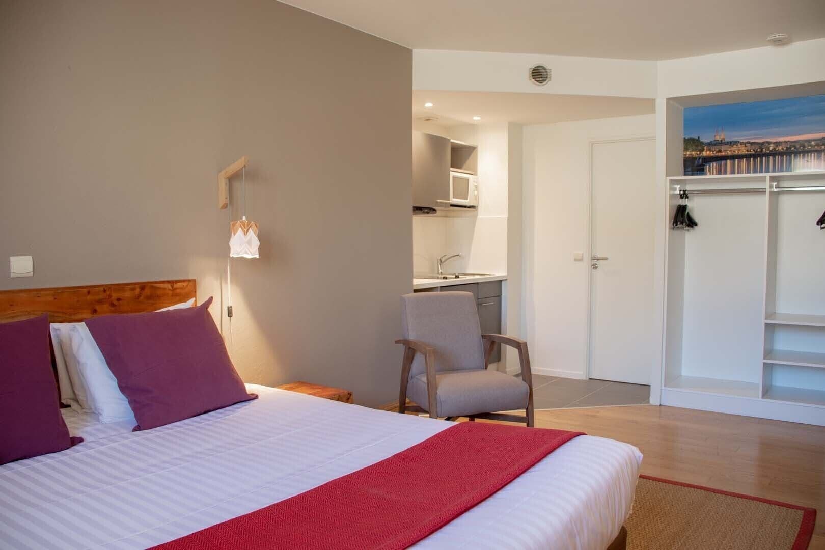 Een slaapkamer met een bed, een stoel, een kast en uitzicht op een stadsgezicht.