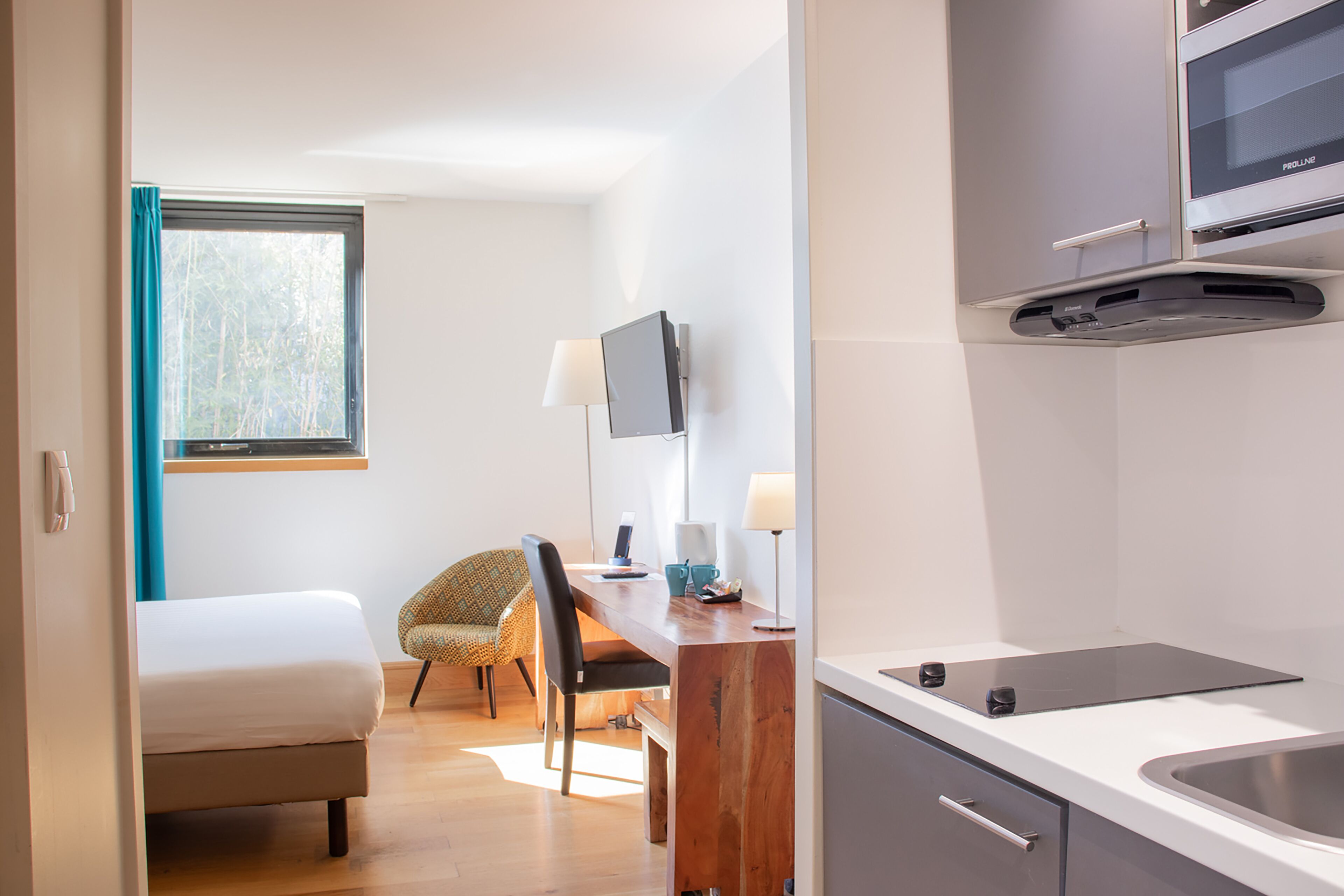 Een moderne hotelkamer met een bed, een bureau met stoel, een televisie en een kitchenette.