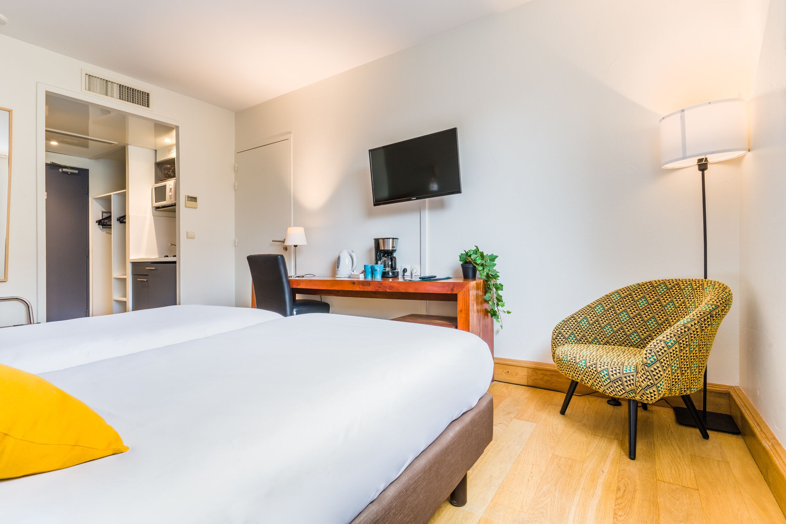 Ein Hotelzimmer mit Bett, Schreibtisch, Stuhl, Fernseher und einer Pflanze.
