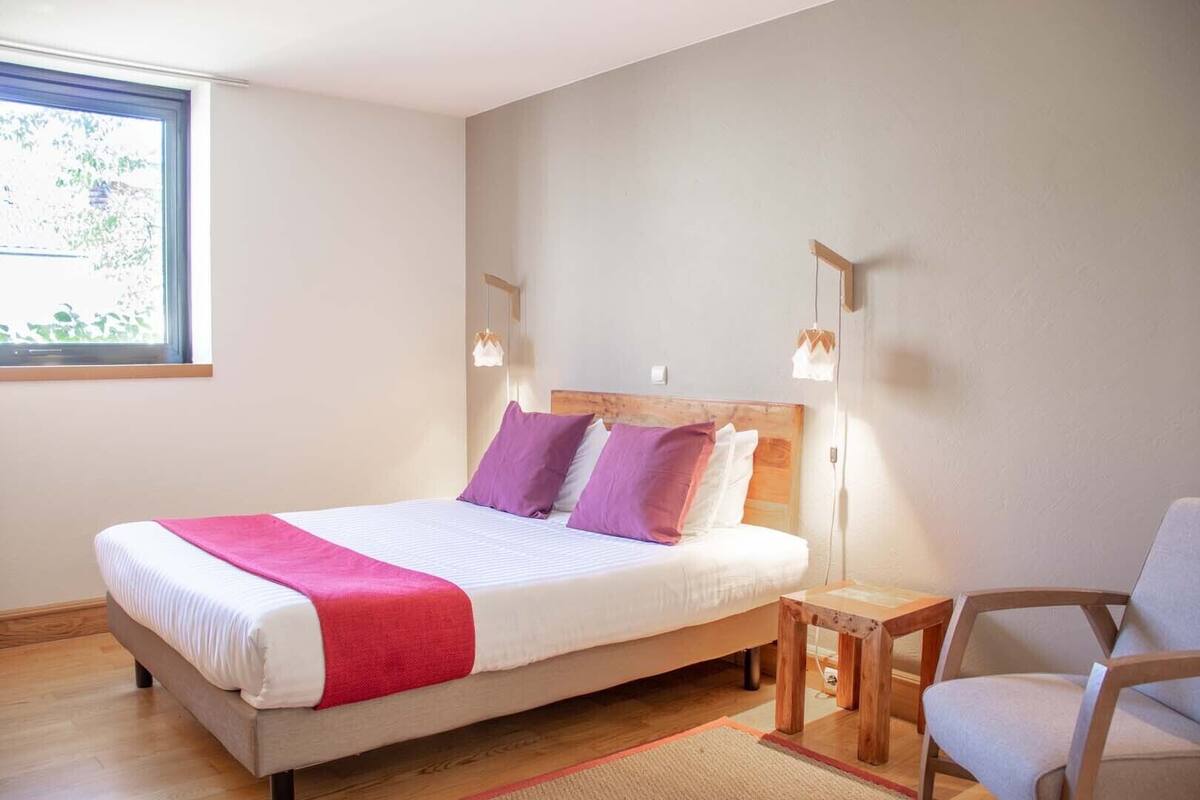 Een slaapkamer met een bed, nachtkastje, stoel en een raam.