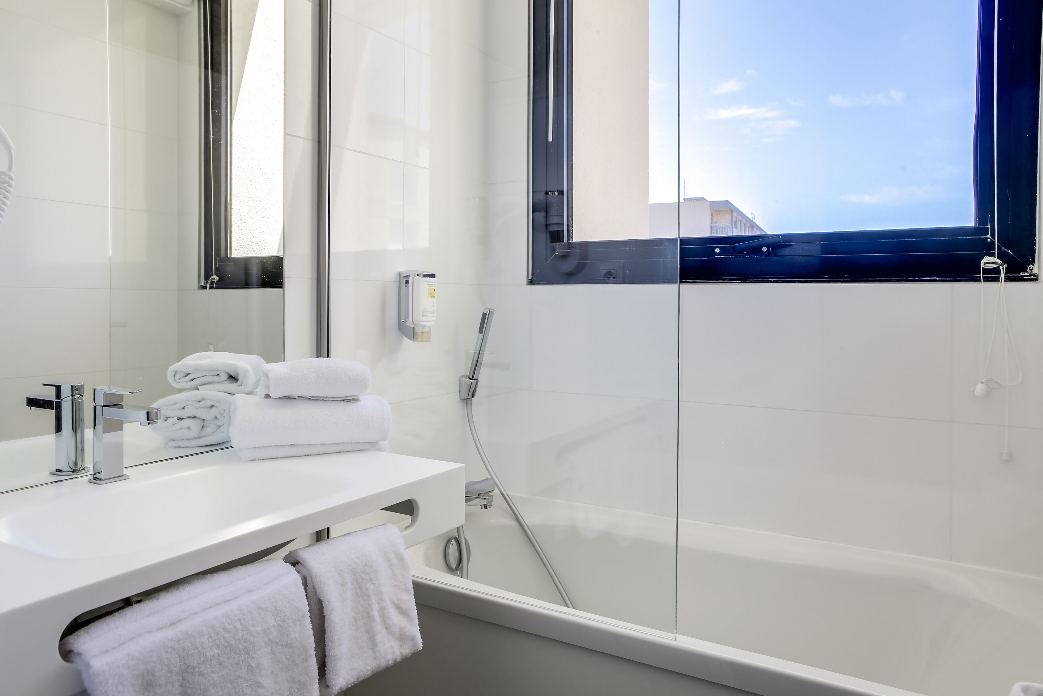 A modern bathroom with a white sink, a mirror, and a glass-enclosed shower.