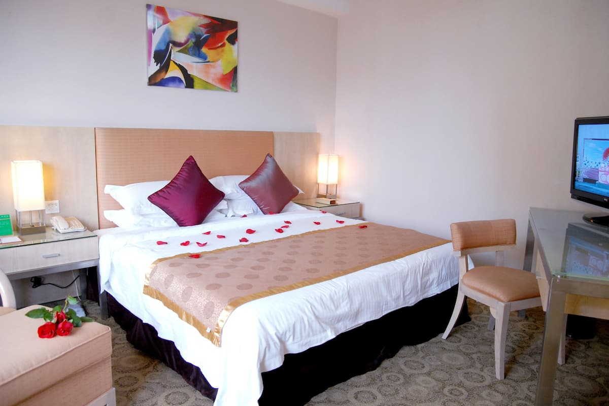 A hotel room with a bed, bedside tables, a desk, a chair, and a television.