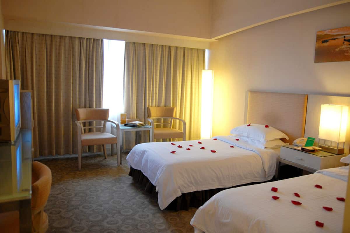 A hotel room with two beds, a desk, a chair, a lamp, and a large window with curtains.