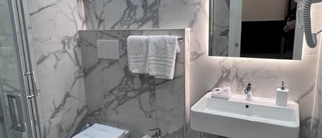 Un baño moderno con ducha de vidrio, un bidé, un lavamanos y un espejo con secador de pelo.