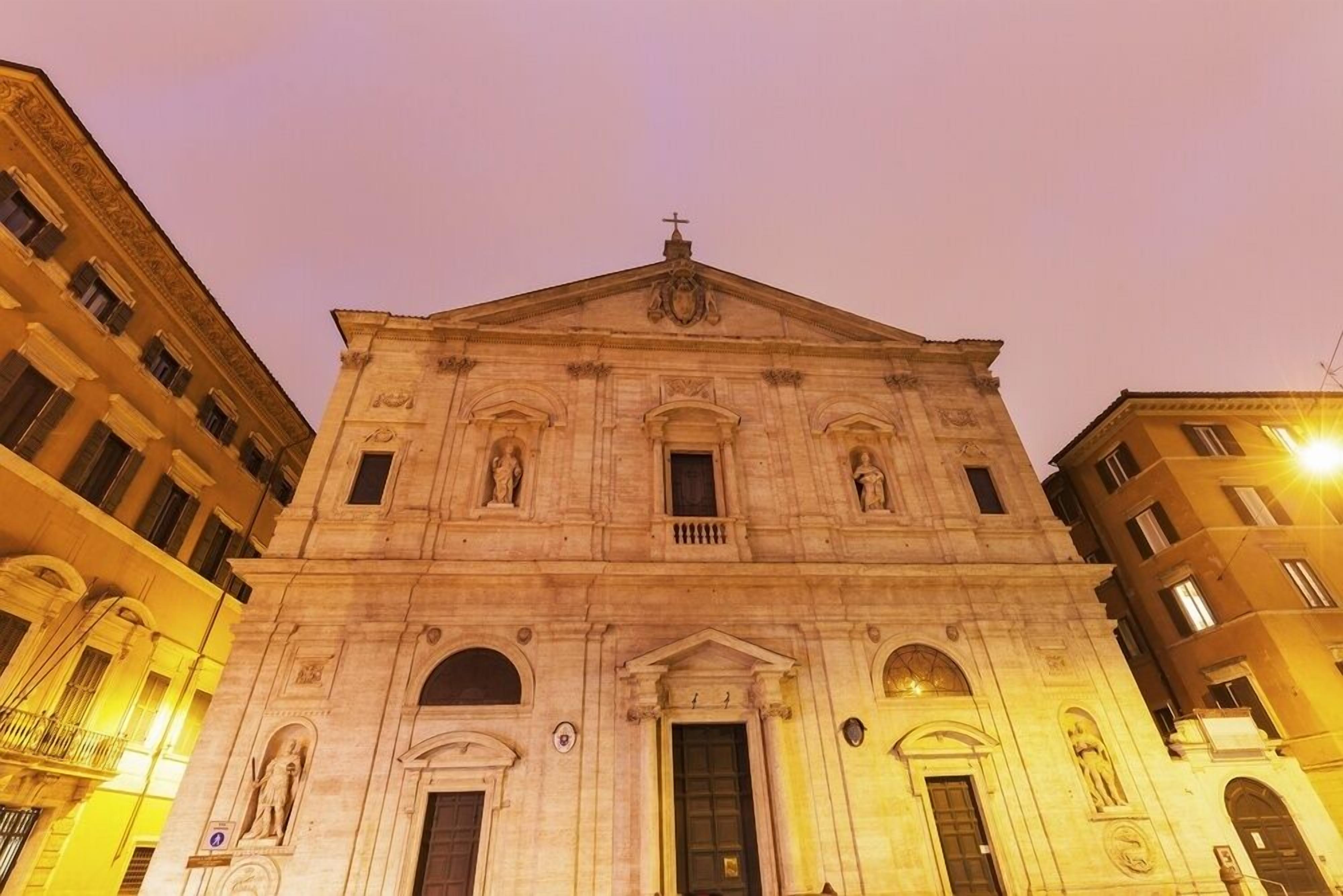 A historic building with a central entrance, flanked by two wings, and a cross on top.
