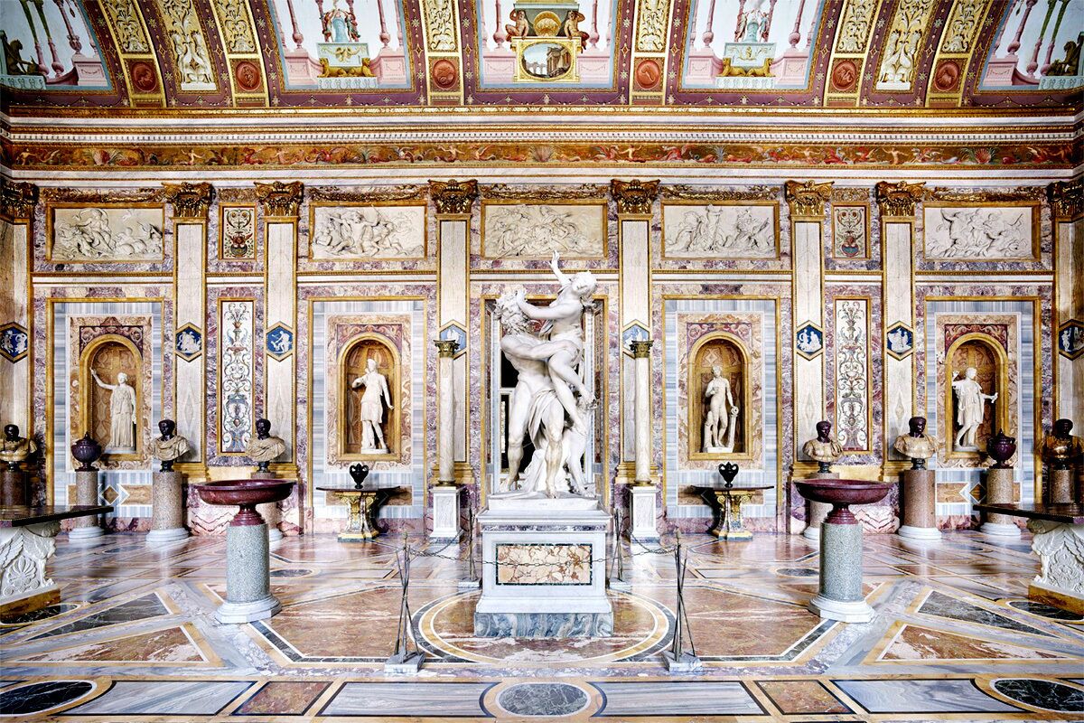 Un salón imponente con una estatua central, columnas ornamentales y decoraciones murales detalladas.