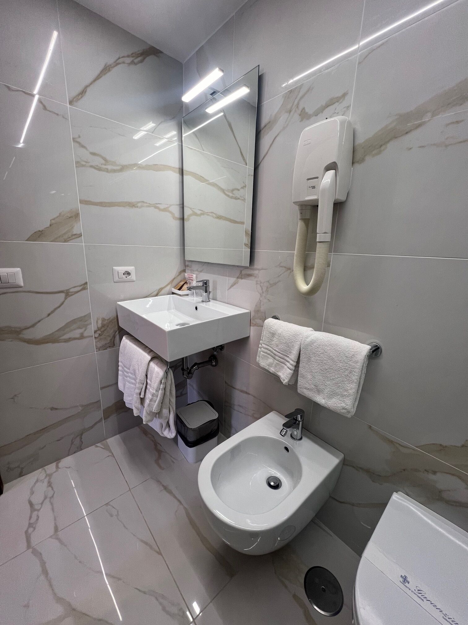 Ein modernes Badezimmer mit Marmorfliesen, einem Standwaschbecken, einem Bidet und einer Toilette.