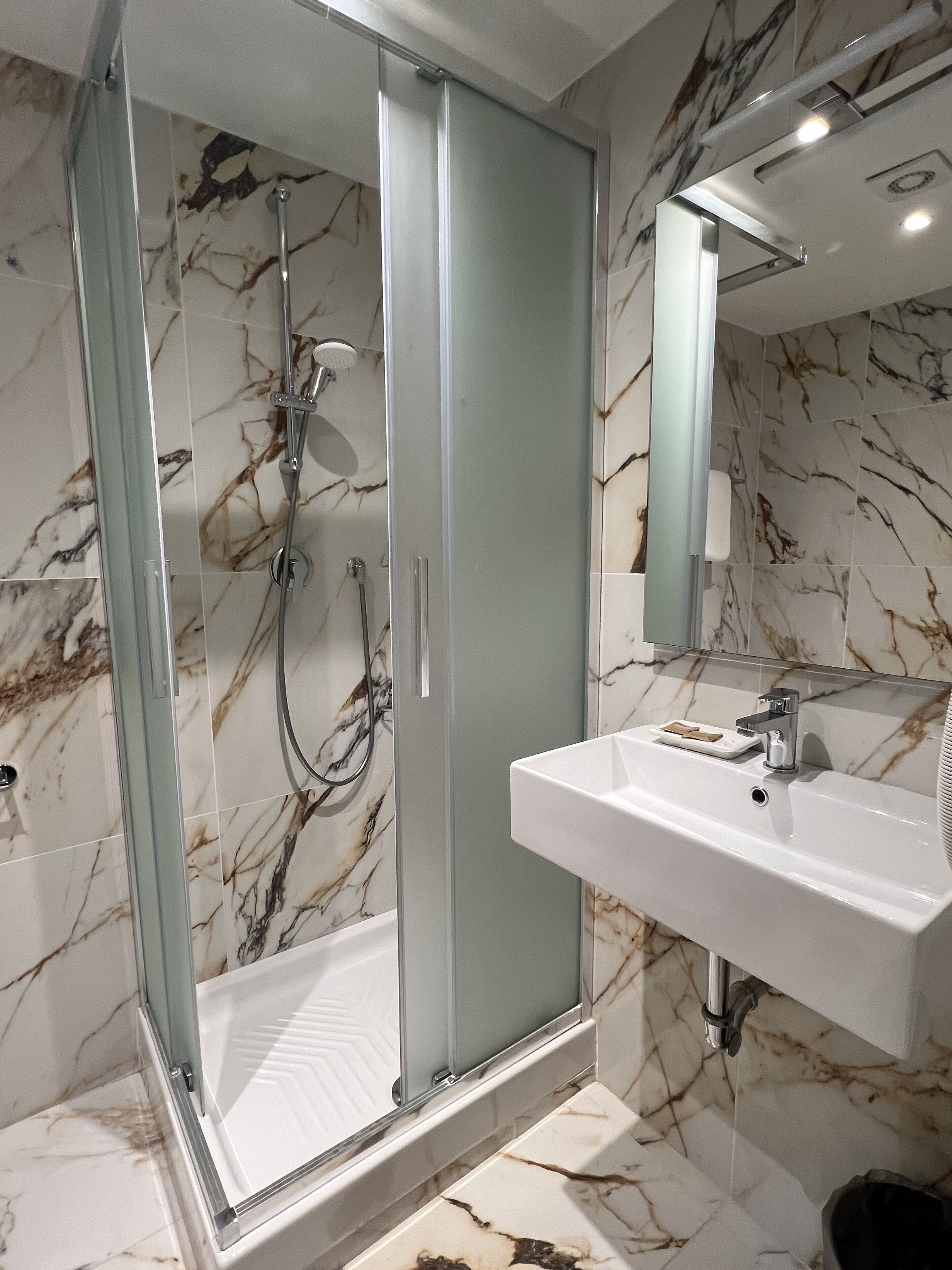 A modern bathroom with a glass-enclosed shower, a white sink, and marble-patterned walls.