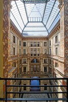 A grand atrium with a glass ceiling, ornate wall decorations, and a central staircase.