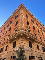 Un edificio de esquina con arquitectura clásica, que destaca por un balcón prominente y numerosas ventanas.