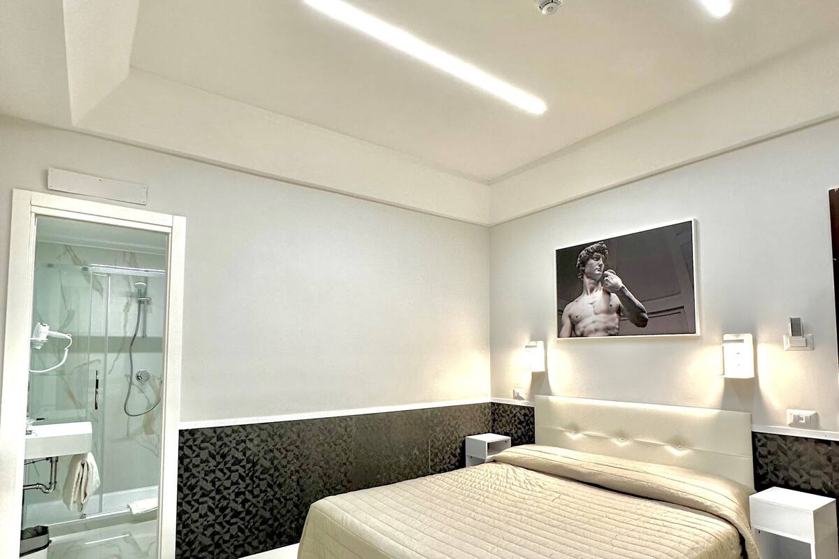 A modern bedroom with a large bed, a glass shower enclosure, and a marble floor.